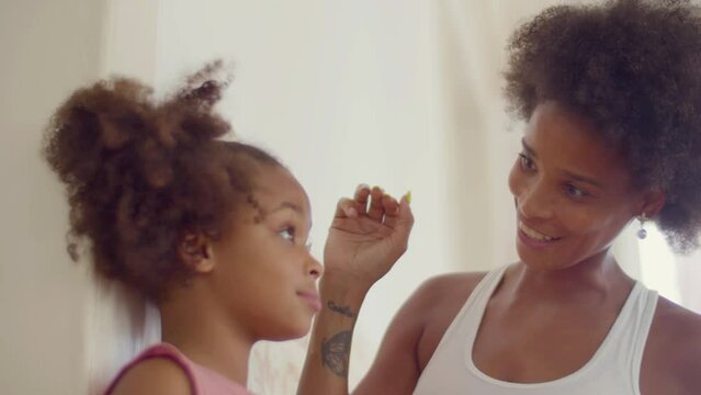 Happy Black woman measuring her daughters height at the wall using pencil. Young mother getting excited with girls growth, showing child mark on the wall. Closeup shot. Parenthood, childhood concept.