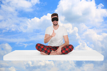 Healthy sleep. Man showing thumbs up on comfortable mattress in blue sky