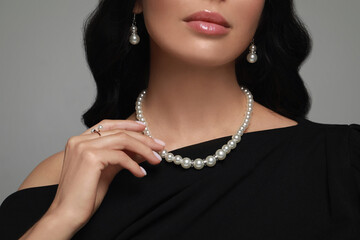 Young woman wearing elegant pearl jewelry on grey background, closeup