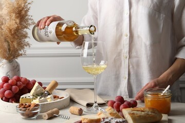Woman pouring white wine from bottle into glass at table with snacks, closeup