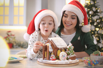 Mother and daughter decorating gingerbread house at table indoors
