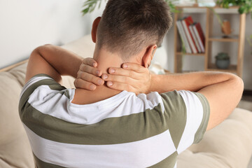 Man suffering from neck pain indoors, back view