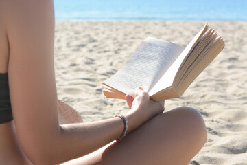 Woman reading book on sandy beach near sea, closeup