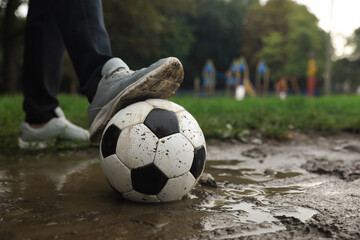 Man with dirty soccer ball in puddle outdoors, closeup