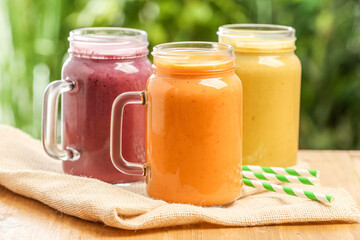 Different delicious smoothies in mason jars on wooden table against blurred background