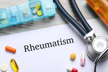 Paper with word Rheumatism, stethoscope and pills on table, closeup