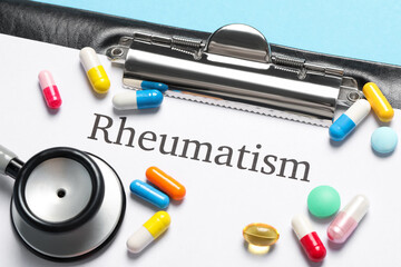 Clipboard with word Rheumatism, stethoscope and pills on light blue background, closeup