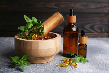 Wooden mortar with fresh green herbs, extracts and capsules on light grey table