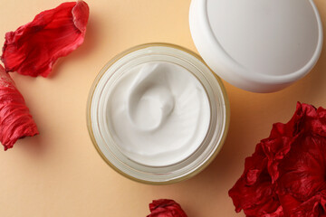 Jar of face cream and red flower petals on beige background, flat lay