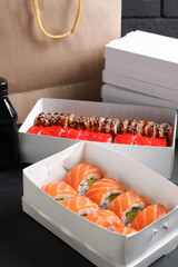 Food delivery. Boxes with delicious sushi rolls, paper package and soy sauce on black table