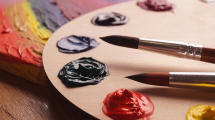 Artist's palette with samples of colorful paints and brushes on wooden table, closeup