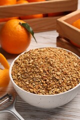 Bowl with dried orange seasoning zest and fruits on white wooden table, closeup