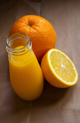 Fototapeta na wymiar an open glass bottle with orange juice and a juicy half of an orange on a light brown background - vertical photo