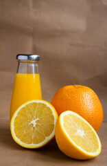 vertical photo - a bottle of orange juice with and two halves of a cut orange and the fruit itself on a light brown blurred background