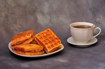 A plate with several Viennese waffles and a cup of hot tea on a gray abstract background.
