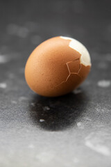 Jajko ugotowane na twardo z pękniętą skorupką na czarnym blacie - obrazy, fototapety, plakaty