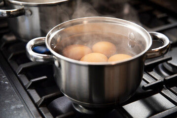 Jajka gotujące się w małym garnuszku ze stali nierdzewnej na czarnej kuchence gazowej - obrazy, fototapety, plakaty