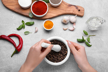 Woman grinding peppercorns in mortar at light grey table, top view