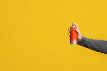 Man holding can of spray paint on yellow background, closeup. Space for text