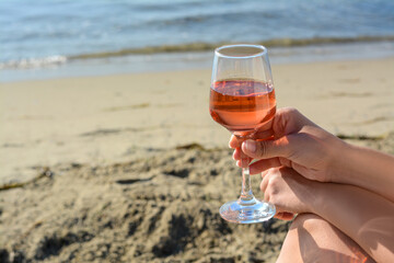 Woman with glass of tasty rose wine near sea, closeup. Space for text