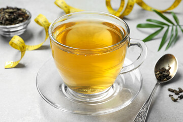 Cup of herbal diet tea and measuring tape on white table, closeup. Weight loss concept