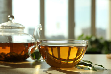Fresh green tea in glass cup, leaves and teapot on table indoors
