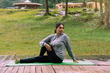 Fototapeta na wymiar Woman alone in a forest practicing yoga in a forest, wearing sportswear and a mat.