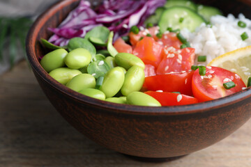 Poke bowl with salmon, edamame beans and vegetables on wooden table, closeup