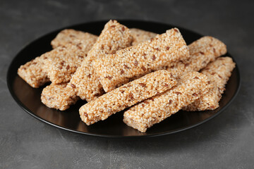 Plate with tasty sesame seed bars on dark grey table, closeup