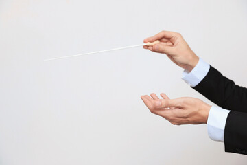 Professional conductor with baton on light grey background, closeup. Space for text
