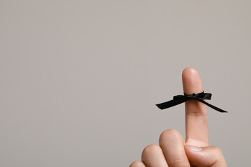 Man showing index finger with black tied bow as reminder on light grey background, closeup. Space for text