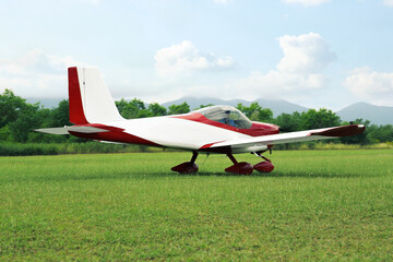 Fototapeta na wymiar Ultralight aircraft on green grass near trees