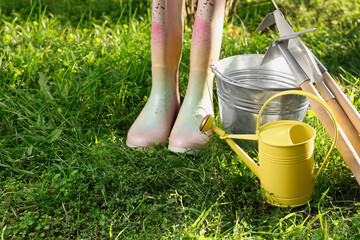 Fototapeta premium Watering can, gardening tools and rubber boots on green grass outdoors