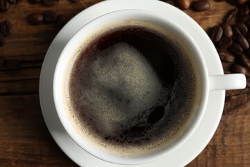 Cup of aromatic coffee on wooden table, top view