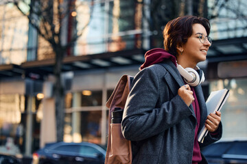Young happy woman with backpack and notebooks going on lecture at university.