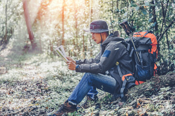 Young male traveler with backpack checks map to find directions in wilderness forest area . Tourist traveler hiker on background landscape view.