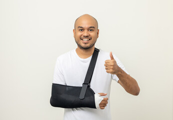 Happy young asian man broken arm with thumbs up on background. Asian man put on plaster bandage...