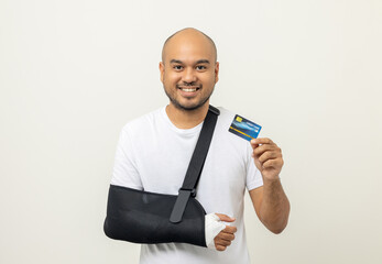 Young asian man broken arm holding credit card payment. Man put on plaster bandage cast splint. Male patient wearing sling support arm after accident injury. Financial life insurance and accident