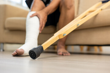 Man suffer pain from accident fracture broken bone injury with leg splints in cast neck splints collar sling support arm walking at home with crutch. Social security and health insurance concept.