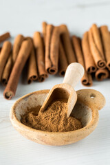 A bowl of cinnamon powder with a pile of cinnamon sticks in behind.