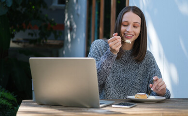 Happy young woman enjoy eating cake while sitting at outdoor cafe.