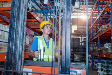 Portrait of a forklift driver wearing a hardhat and vest while moving stock around the floor of a...