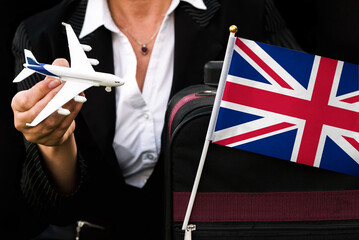 business woman holds toy plane travel bag and flag of United Kingdom
