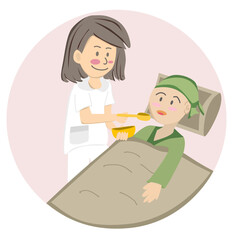 A nurse is feeding a cancer patient who is lying in bed.