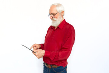 Pleased senior man using tablet. Happy Caucasian male model with gray hair and beard in red shirt and glasses looking down, smiling, touching screen. Modern technology, advertisement concept