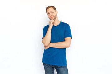 Fototapeta premium Pensive man thinking and touching chin with hand. Caucasian man looking up, considering ideas, brainstorming, while standing on white background. Imagination, wonder, inspiration concept