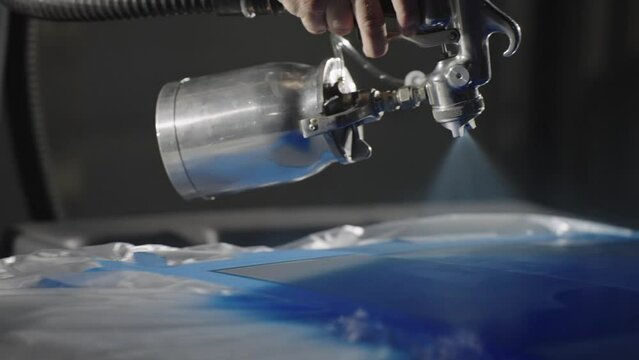Close up, spray paint gun painting metal in blue. Handheld slow motion