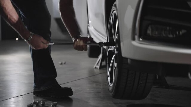 Unrecognizable mechanic removing lug nuts from car wheel with lug wrench, slow motion