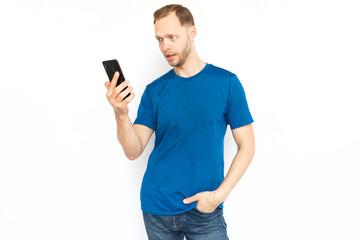 Shocked man looking at mobile phone screen. Surprised bearded man receiving bad or good news, standing on white background, posing for camera. Emotion, surprise, frustration concept