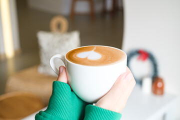 Beautiful girl in green sweater holding cup of tea or coffee in the morning. Closeup of female hands holding a mug of beverage.